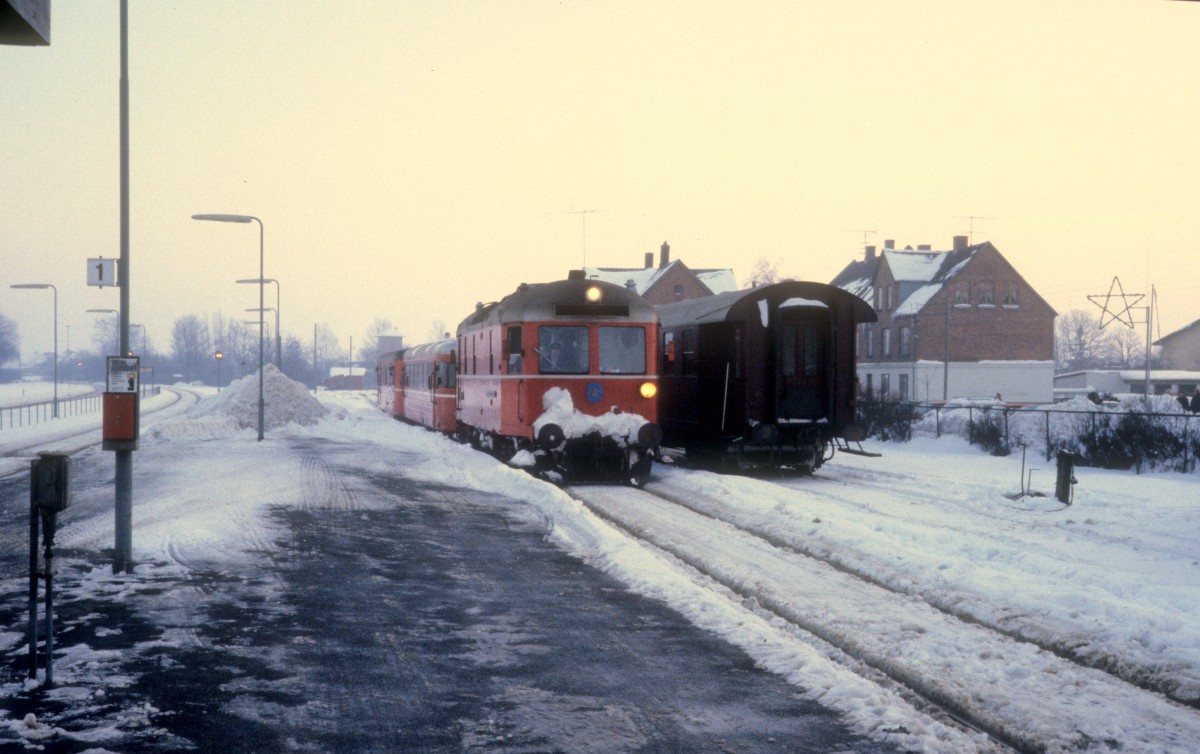 OHJ-Diesellok 24, die einen Triebzug bestehend aus dem HTJ-Triebwagen S 44 und dem OHJ-Postwagen D 246 schleppt, erreicht am 28. Dezember 1981 den HTJ-Bahnsteig im Bahnhof Tølløse. - Der Triebzug war wegen heftigen Schneefalles auf der Bahnstrecke Høng - Tølløse - Slagelse (HTJ) im Schnee stecken geblieben und musste deshalb von der Diesellok abgeholt werden. Der Zug ist auf dem Weg zur HTJ/OHJ-Werkstatt in Holbæk.