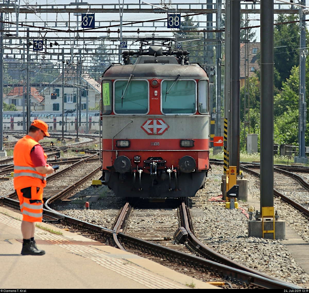 Orange in verschiedenen Farbtönen...
Aug' in Aug' mit Re 4/4 II 11108 (420 108-3) SBB, in ehemaliger  Swiss Express -Farbgebung, die mit drei Einheitswagen I (Wagen für NPZ) der SBB im Bahnhof Biel/Bienne (CH) abgestellt ist.
Der links angedeutete Bahnmitarbeiter scheint aufgrund dieses Zuges dort anwesend zu sein.
[24.7.2019 | 13:19 Uhr]