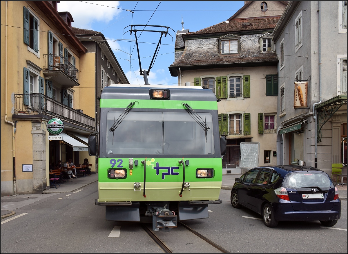 Ortsdurchfahrt in Bex. Das Auto ist in Sicherheit gebracht, es kommt TPC-Triebwagen 92 der Bex–Villars-sur-Ollon–Bretaye-Bahn entgegen. Juli 2017.

Für Zweifler: Standort des Fotografen ist der Bahnsteig Place du Marché.
