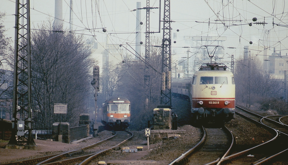 Paralleleinfahrt von 103 240-8 mit einem IC und eines Nahverkehrszuges mit führendem Steuerwagen um 1980 in den Bahnhof Köln-Deutz. Heute ist die im Hintergrund sichtbare Industriekulisse komplett verschwunden.