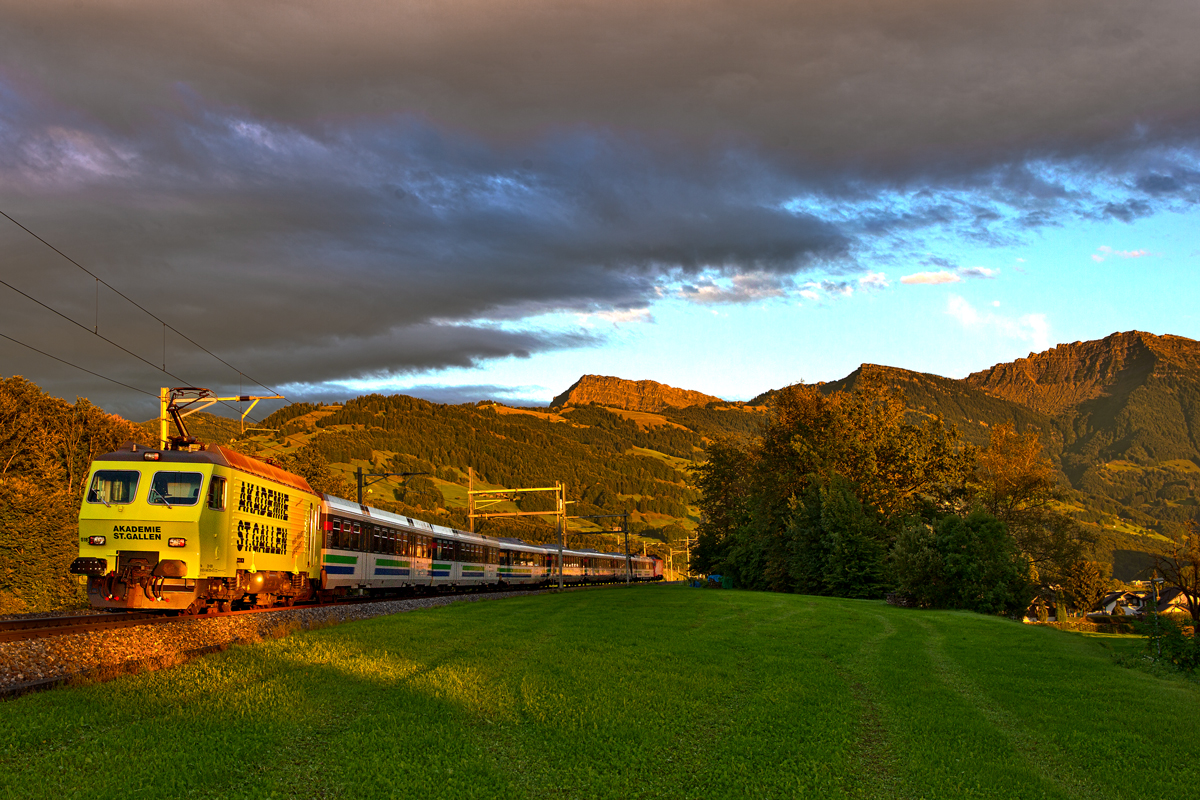 Passend zum Abendrot(wie Bonbonfarben aber nicht zu vermeiden in den Alpen) bei einer föhnigen Aufhellung schiebt die giftgelb neulackierte SOB Lokomotive RE 456 018  Akademie St.Gallen  am VAE.Bild Kaltbrunn den 17.9.2015