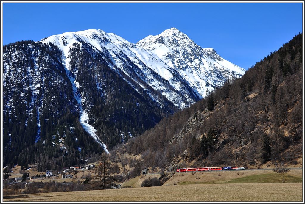 R1929 Nach Pontresina zwischen Sagliains und Susch mit Piz Linard 3410m. Schiebende Lok ist die Ge 4/4 II 627  Reichenau-Tamins  mit der 100 Jahre Chur-Arosa Eigenwerbung. (10.04.2015)