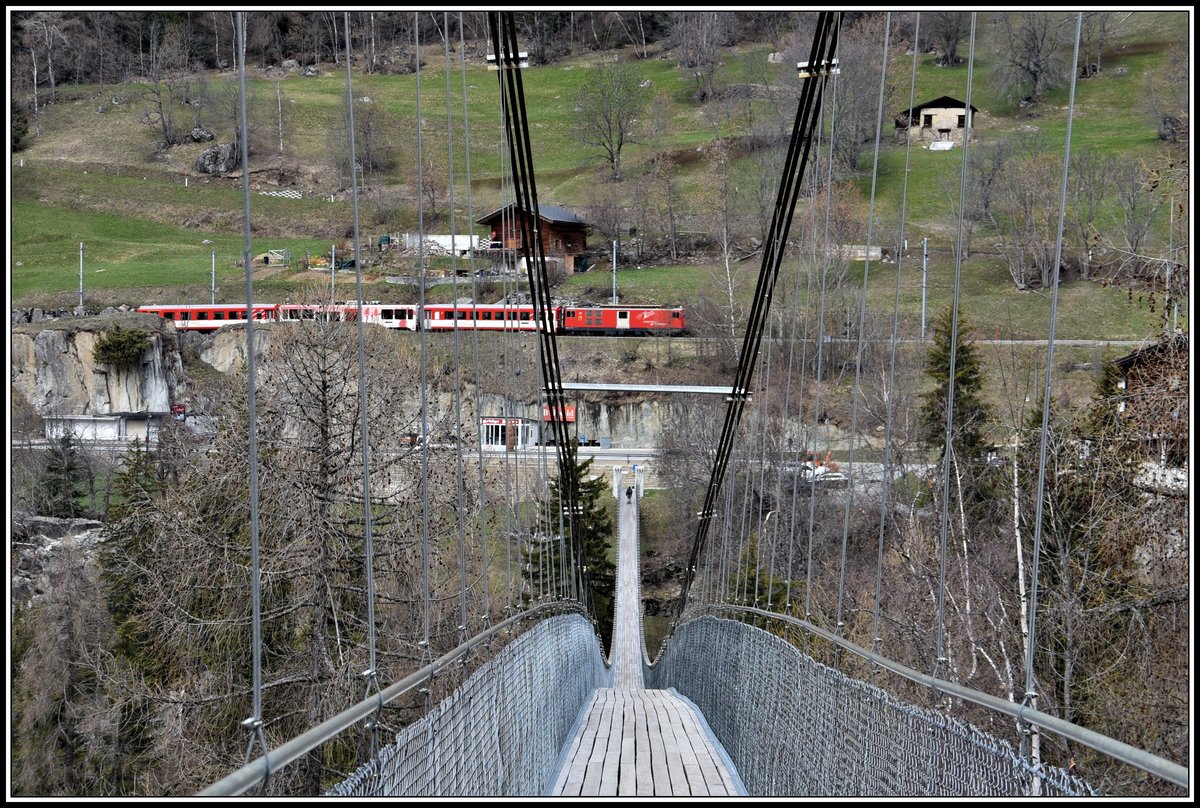 R530 mit Deh 4/4 II nach Andermatt passiert die Hängebrücke, die Fürgangen-Bellwald mit Mühlebach verbindet. 280m lang und 92m hoch. (16.04.2019)