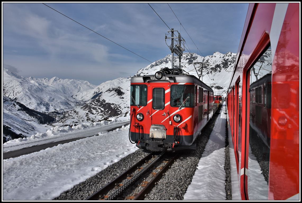 R823 kreuzt in Nätschen einen Autozug nach Sedrun mit einem Deh 4/4. Im Hintergrund ist das Urserental mit Hospental und Realp zu sehen. (16.04.2019)