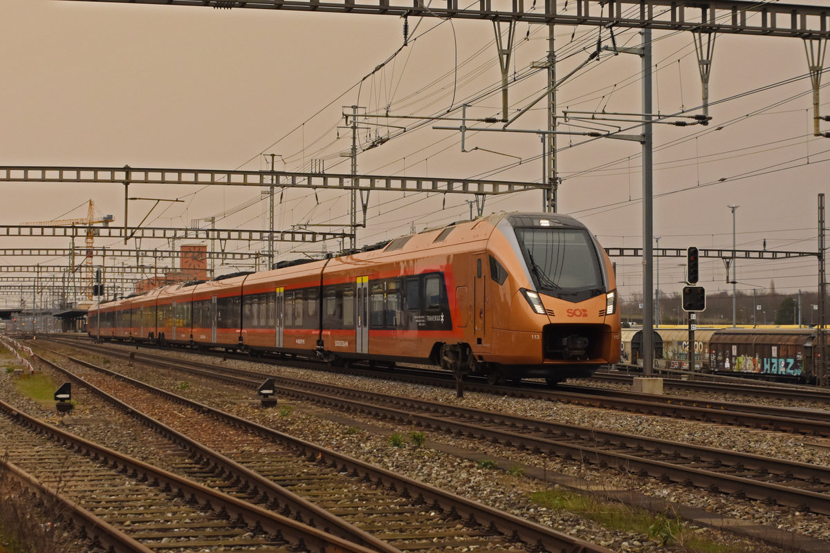 RABe 526 113 Traverso der SOB durchfährt den Bahnhof Muttenz. Der Himmel ist vom Saharasand rot gefärbt. Die Aufnahme stammt vom 06.02.2021.