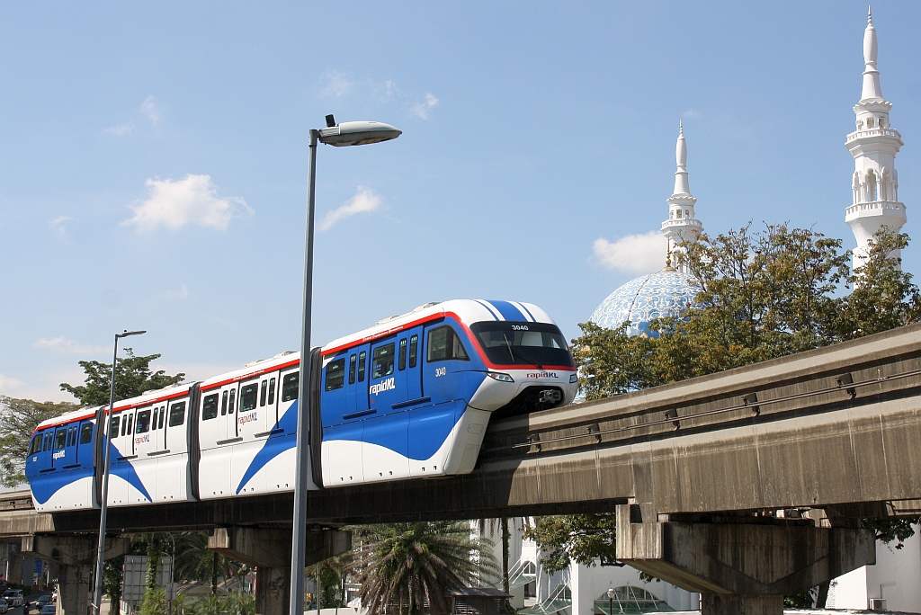 rapidKL Monorail Garnitur 30 mit den Nummern 3037 - 3040 (Hersteller: Scomi Rail, Type SUTRA) am 13.Dezember 2023 zwischen den Stesen's BBCC-Hang Tuah (MR4) und Maharajalela (MR3). - Die beiden Minarette im Hintergrund gehören zur Al-Bukhary Moschee.