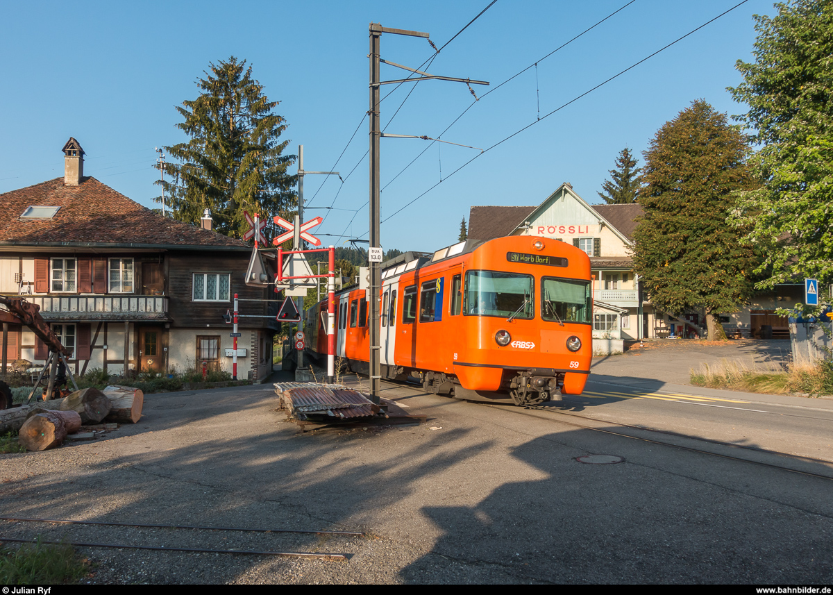 RBS Mandarinli Be 4/12 59 mit Schwesterfahrzeug am Morgen des 28. August 2018 in Boll. Nicht nur die Mandarinli werden bald verschwinden, auch die Ortsdurchfahrt Boll mit den drei unbeschrankten Bahnübergängen soll in den nächsten Jahren verlegt werden.
Die Feldbahngleise unten rechts gehören zu einer Sägerei.
