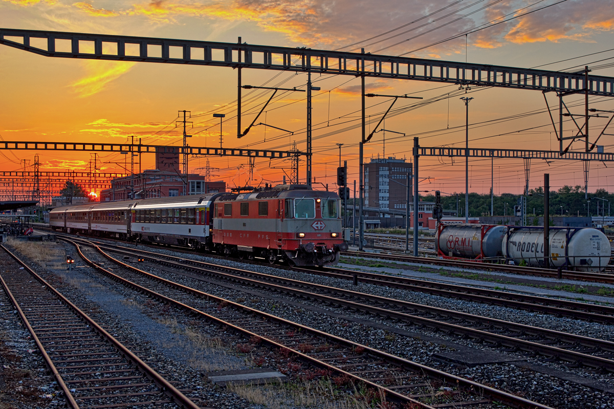 Re 4/4 II 11106 fährt bei Sonnenuntergang mit einem Ec in Muttenz vorüber.Bild vom 11.6.2015