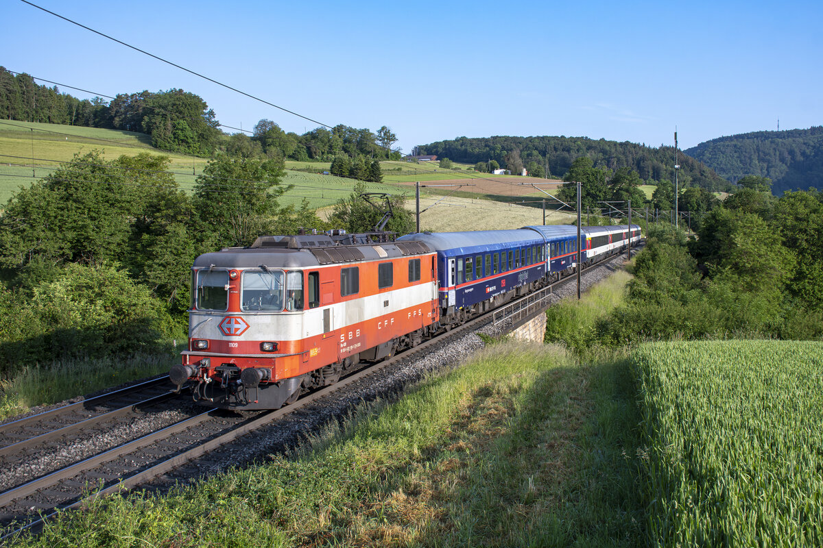 Re 4/4 II 11109 ist mit dem NJ 403 aus Amsterdam unterwegs in Richtung Zürich. Aufgenommen in Hornussen AG am Morgen des 29.05.2023.