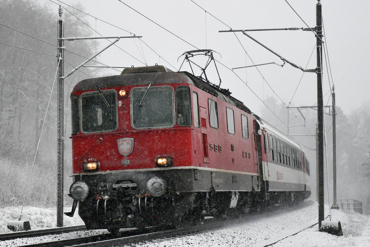 Re 4/4 II 11112 ist am 27.02.2020 bei winterlichen Verhältnissen mit einem Interregio auf der Bözbergrampe bei Schinznach-Dorf unterwegs in Richtung Basel.