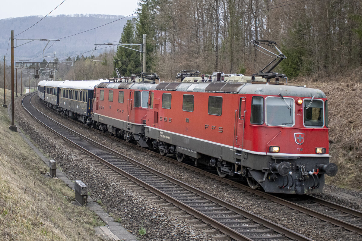 Re 4/4 II 11191 und 11199 sind im Wald zwischen Rupperswil und Lenzburg mit dem VSOE unterwegs in den Süden, aufgenommen am 29.03.2022.