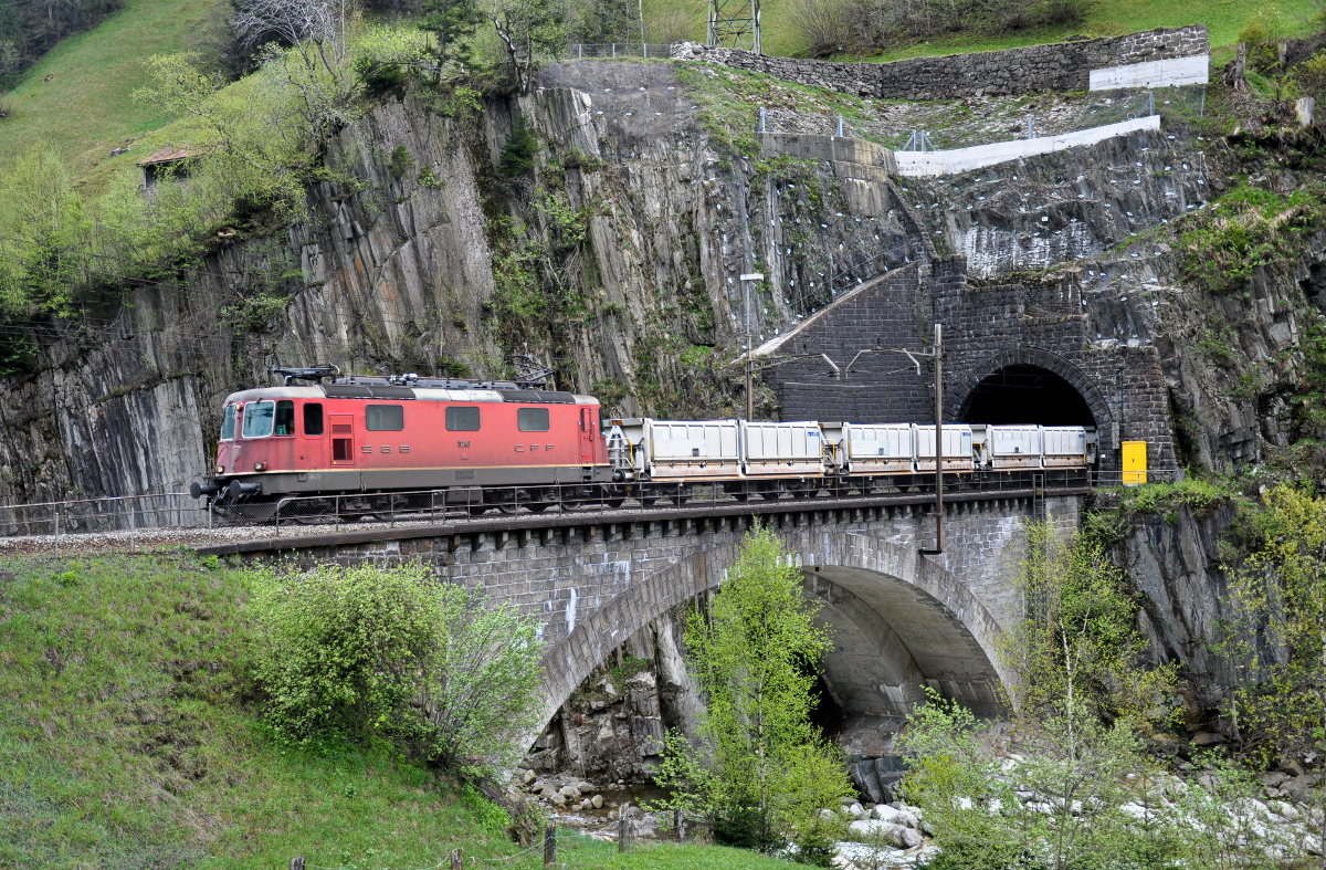 Re 4/4 II 11246 führt einen Güterzug bestehend aus Aushubwagen aus dem Wattinger-Kehrtunnel über die untere Wattinger-Brücke und weiter den Gotthard hinuntern. Aufgenommen am 28.04.2015 bei Wassen