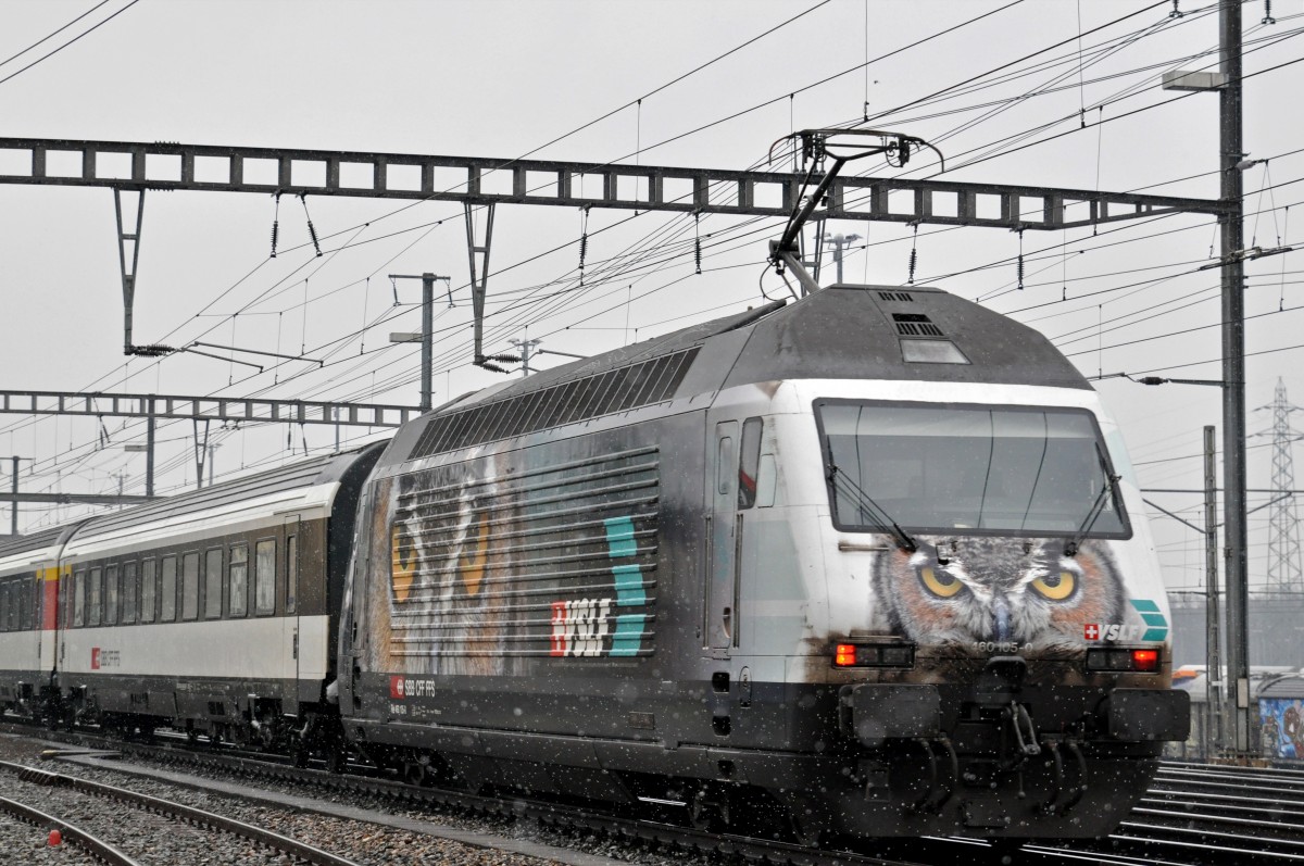 Re 460 105-0 mit der VSLF Werbung durchfährt bei leichtem Schneefall den Bahnhof Muttenz. Die Aufnahme stammt vom 26.01.2015.