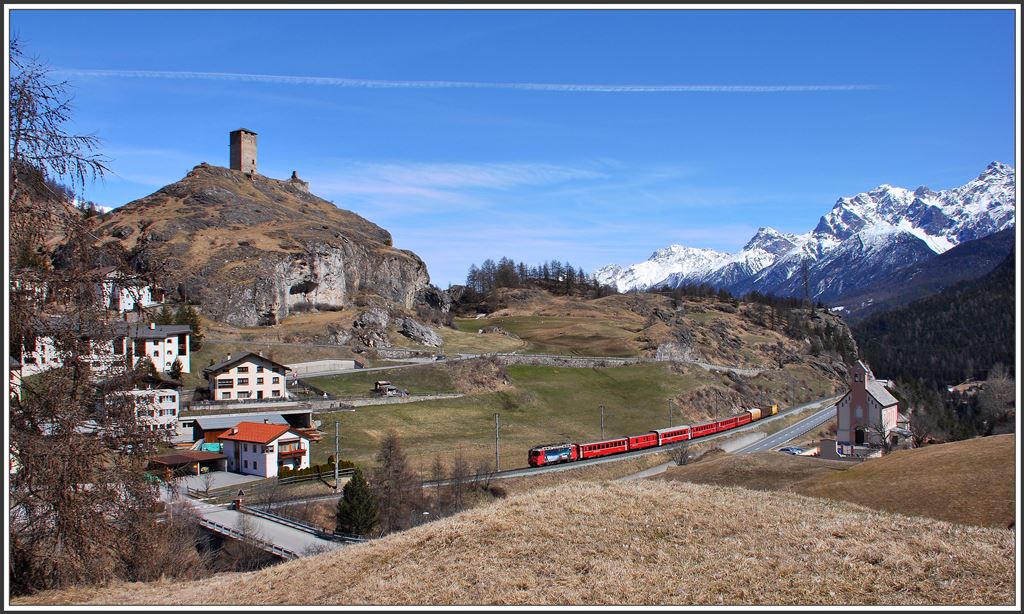 RE1244 von Scuol-Tarasp nach Disentis/Mustér erreicht Ardez. Mit dreieinhalb Stunden ist es neben dem Berninaexpress der längste durchgehende Zuglauf der RhB. Zuglok ist die Ge 4/4 II 615  Klosters . Auf dem Hügel thront die Ruine Steinsberg und am Dorfrand steht die Katholische Kirche. (09.04.2015)
