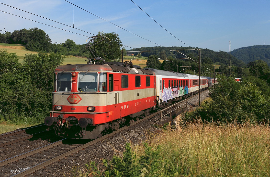 Re4/4 11109 erklimmt mit Nachtzug 458 die Steigung am Bözberg zwischen Hornussen und Zeihen. Die Lackierung ist ein Relikt des kurzlebigen Swiss-Express Systems der 1980er Jahre. Nun wird das Fotografenglück, diese Lok vor dem 458 zu erwischen, doch arg getrübt durch das Graffito auf dem ersten Wagen ...