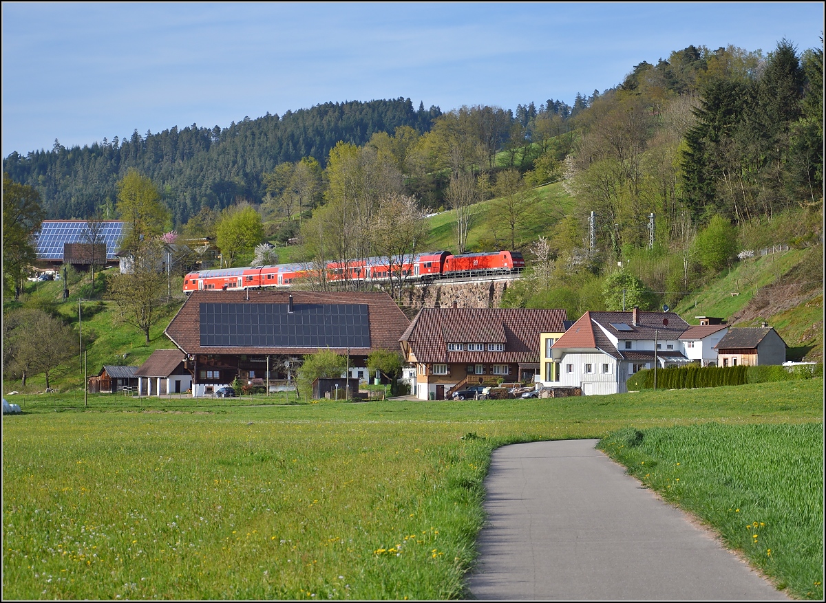 Regionalexpress in Gutach mit 146 230-8. Wie die Orgelpfeifen sind diese drei Schwarzwaldbauernhöfe an der Strecke aufgereiht. April 2015.