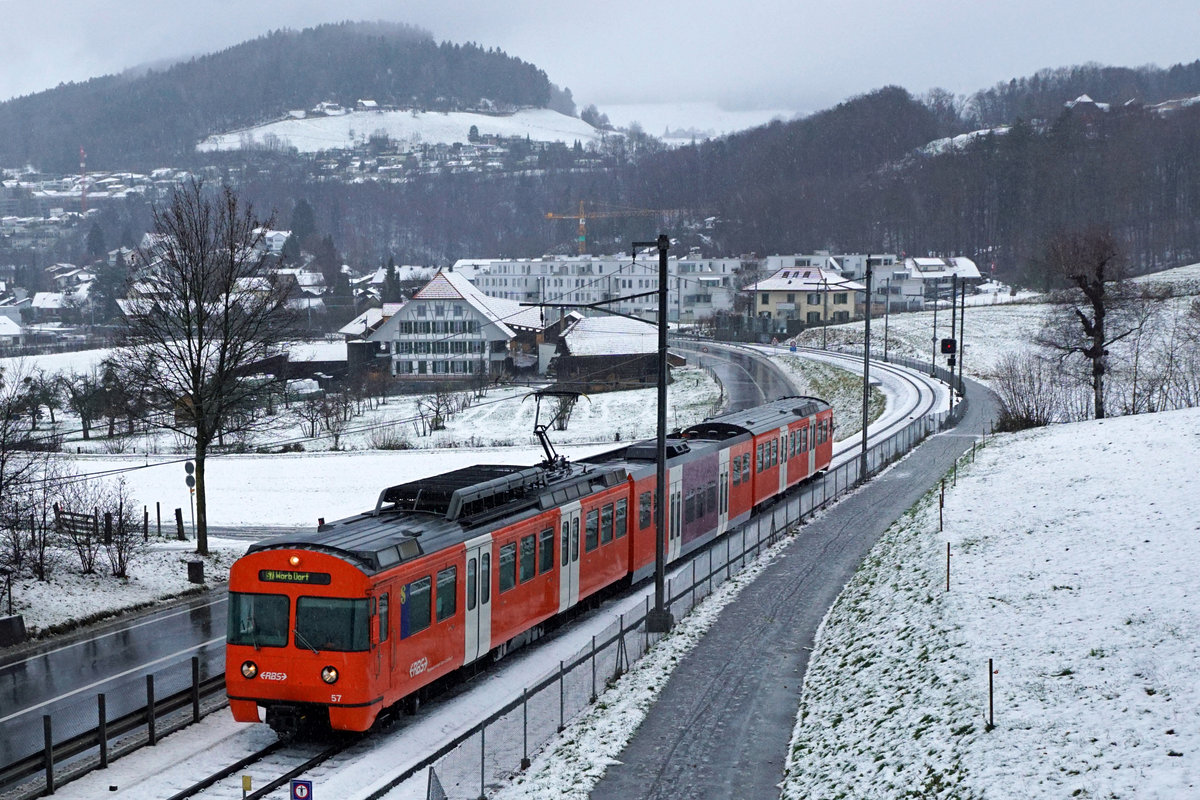 Regionalverkehr Bern Solothurn/RBS.
MANDARINLI  ADIEU.
Nach 45 Dienstjahren haben die bekannten Mandarinli, wie sie im Volksmund heissen ausgedient.
Während diesen vielen Jahren prägten sie das Bild sehr stark im Worblental auf der S 7 Bern – Worb Dorf. In der Woche vom  11. Bis zum 15. Dezember 2019 standen sie ein letztes Mal im Plandienst, damit sich die Fahrgäste und die Eisenbahnfreunde von ihnen verabschieden konnten.  Die beiden letzten Triebzüge Be 4/12 56 und Be 4/12 57 werden zwar vorerst nicht verschrottet, da sie noch als eiserne Reserve zurückbehalten werden. Da ich zusammen mit diesen eleganten orangen Triebzügen den grössten Teil  meines Lebens verbringen  konnte, freue ich mich über sehr viele Abschiedsbilder unter BB.de.  Ich werde meinen Beitrag leisten. Ich verabschiedete mich am Freitag den 13. Dezember 2019 zusammmen mit mehreren Bahnfreunden.  
So himmeltraurig das Wetter, so traurig der Abschied von diesem Zug.  Nicht nur das Taschentuch sondern auch meine Kleider waren durch und durch nass.
Mandarinli adieu!
Foto: Walter Ruetsch

