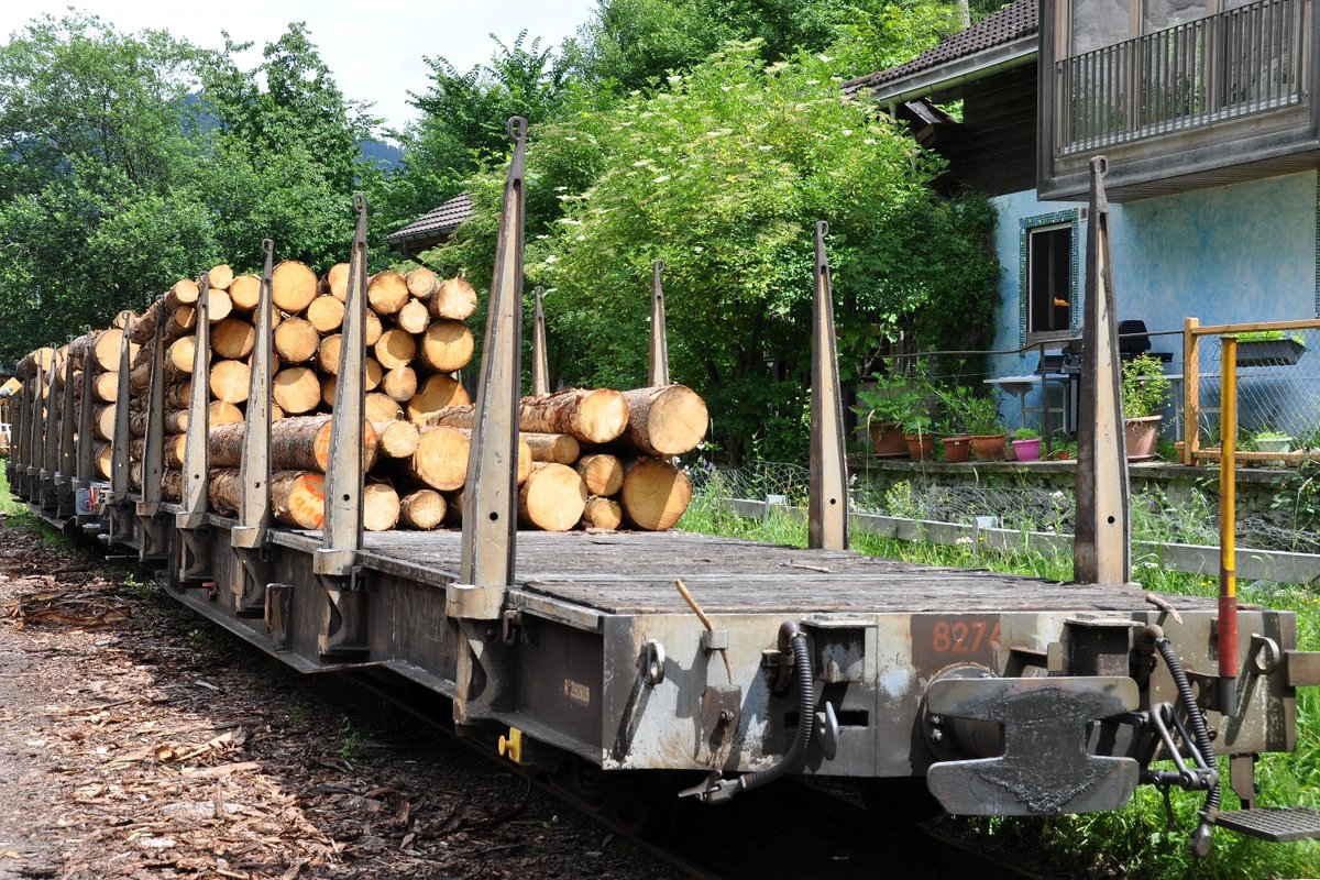 Rhätische Bahn RhB Holztransportwagen Sp-w 8274 am 27.06.2015 in der Station Versam-Safien. Die Waggons stehen auf einem Gleis, das überquert werden muss, um zum eigentlichen, beschrankten Bahnübergang zu gelangen.