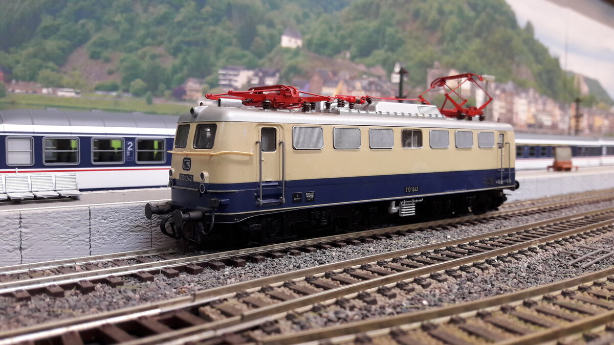 Rheingold Lokomotiven , als E10 Kasten und Bügelfalten E10 ( später 112)….
Die geplante E10 Bügelfalte war noch nicht fertig gestellt, da wurden einige E10 Kasten in Rheingoldlackierung als Provisorium umgebaut….. Provisorium 1 :  6 Loks ( 239-244) mit Getriebumbau auf 160 km/h , sie bekamen eine 1 vor der Ordnungsnummer also E10 1239 -1244 . Die 1244 bekam ein sogenanntes Henschel – Drehgestell was sie auch behielt.
Da die E10 Bügelfalte immer noch nicht fertig war, orderte man nochmal 5 Loks der Kasten E10 nach ( Provisorium 2 )  , welche direkt mit Henscheldrehgestellen ausgeliefert wurden.  E10 250-254 . Diese bekamen keine 1 davor, also wie gehabt E10 250-254 …. Zu unterscheiden waren Provisorium 1 und 2 unter anderem auch an der Beschriftung. Provisorium 1 hatte vorne den DB Keks und an der Seite keinen.  Provisorium 2 umgekehrt, vorne kein Keks, dafür an Seite. …. Ab 1962 gab es dann die ersten Bügelfalten E10 in Rheingoldausführung.  6 Loks  E10 1239-1270, diese hatten keine Rehling vorne .  Ab 1963 dann die nächste Lieferung E10 1308-1012  welche nun aber eine Rehling vorne hatten. Ab 1966 wurden die blau/ elfenbein lackierten Loks in TEE Farben umlackiert. Deswegen gab es auch mit E10  1308  usw , beschriftete E10er Bügelfalten in TEE Farben….1968 gab es dann die 3. Lieferung von 20 Loks  E10 485-504 welche aber direkt als 112 er Loks in TEE Farben ausgeliefert wurden. Alle Kasten Rheingold E10 wurden später wieder in blau zurück lackiert.  Hier das Modell des 1. Provisoriums, Kasten E10, E10 1242, Regenrinne, Rehling vorne, DB Keks vorne und seitlich keinen. Modell Liliput 320511 DC nachdigitalisiert.
