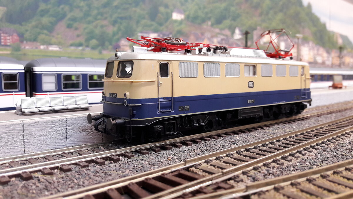Rheingold Lokomotiven , als E10 Kasten und Bügelfalten E10 ( später 112)….
Die geplante E10 Bügelfalte war noch nicht fertig gestellt, da wurden einige E10 Kasten in Rheingoldlackierung als Provisorium umgebaut….. Provisorium 1 :  6 Loks ( 239-244) mit Getriebumbau auf 160 km/h , sie bekamen eine 1 vor der Ordnungsnummer also E10 1239 -1244 . Die 1244 bekam ein sogenanntes Henschel – Drehgestell was sie auch behielt.
Da die E10 Bügelfalte immer noch nicht fertig war, orderte man nochmal 5 Loks der Kasten E10 nach ( Provisorium 2 )  , welche direkt mit Henscheldrehgestellen ausgeliefert wurden.  E10 250-254 . Diese bekamen keine 1 davor, also wie gehabt E10 250-254 …. Zu unterscheiden waren Provisorium 1 und 2 unter anderem auch an der Beschriftung. Provisorium 1 hatte vorne den DB Keks und an der Seite keinen.  Provisorium 2 umgekehrt, vorne kein Keks, dafür an Seite. …. Ab 1962 gab es dann die ersten Bügelfalten E10 in Rheingoldausführung.  6 Loks  E10 1239-1270, diese hatten keine Rehling vorne .  Ab 1963 dann die nächste Lieferung E10 1308-1012  welche nun aber eine Rehling vorne hatten. Ab 1966 wurden die blau/ elfenbein lackierten Loks in TEE Farben umlackiert. Deswegen gab es auch mit E10  1308  usw , beschriftete E10er Bügelfalten in TEE Farben….1968 gab es dann die 3. Lieferung von 20 Loks  E10 485-504 welche aber direkt als 112 er Loks in TEE Farben ausgeliefert wurden. Alle Kasten Rheingold E10 wurden später wieder in blau zurück lackiert.  Hier das Modell des 2. Provisoriums, Kasten E10, E10 253, Regenrinne, keine Rehling vorne, DB Keks vorne fehlt, dafür seitlich aufgebracht. Dieses Modell ist ein Unikat, in dieser Version von keinem Hersteller in H0 gebracht. Angefertigt wurde die Lok vom Lokpainter Bart.  Grundmodell Roco , DC digital