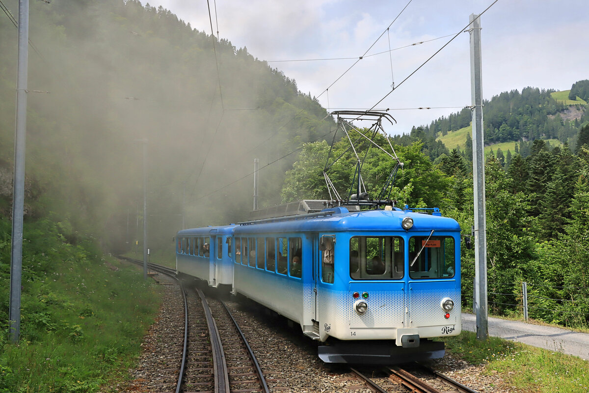 Rigi Bahn Arth-Goldau - Rigi Kulm: Triebwagen 14 (1967) + Steuerwagen 24 (1967) überholt und verschwindet im Rauch des wartenden Dampfzugs mit der Stehboilerlokomotive 7 in Fruttli. 24.Juli 2021. Fotostandort: Nachdem der historische Dampfzug der Rigi Bahn auf das bergseitige Gleis gewechselt hatte, damit der überholende Zug mit Triebwagen 14 am Bahnhof Fruttli halten konnte, habe ich die Aufnahme bei dessen Weiterfahrt aus dem offenen Wagen Nr.11 gemacht, nach oben hinausschauend. 