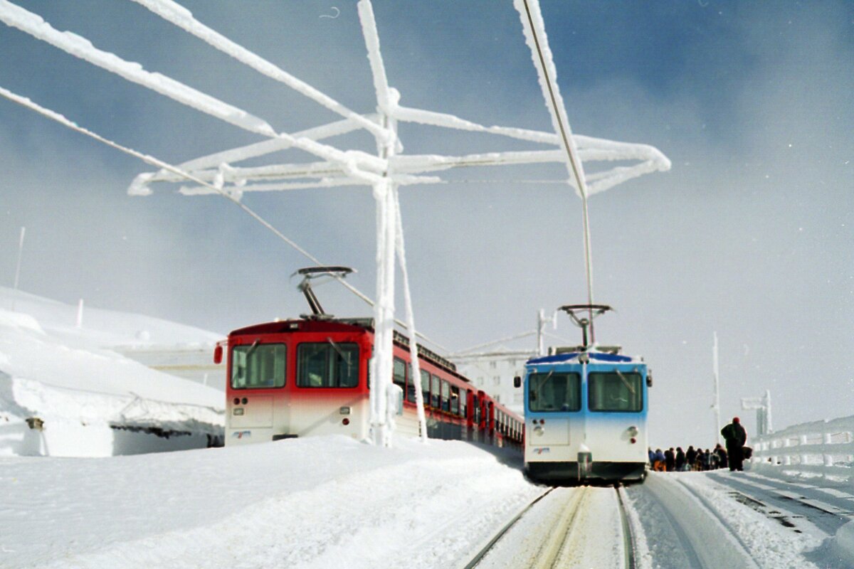 Rigi Zahnradbahnen_02-2005_Endbhf. Rigi-Kulm. Einträchtig nebeneinander Zug der Vitznau-Rigi-Bahn (rot) und der Goldau-Rigi-Bahn (blau).