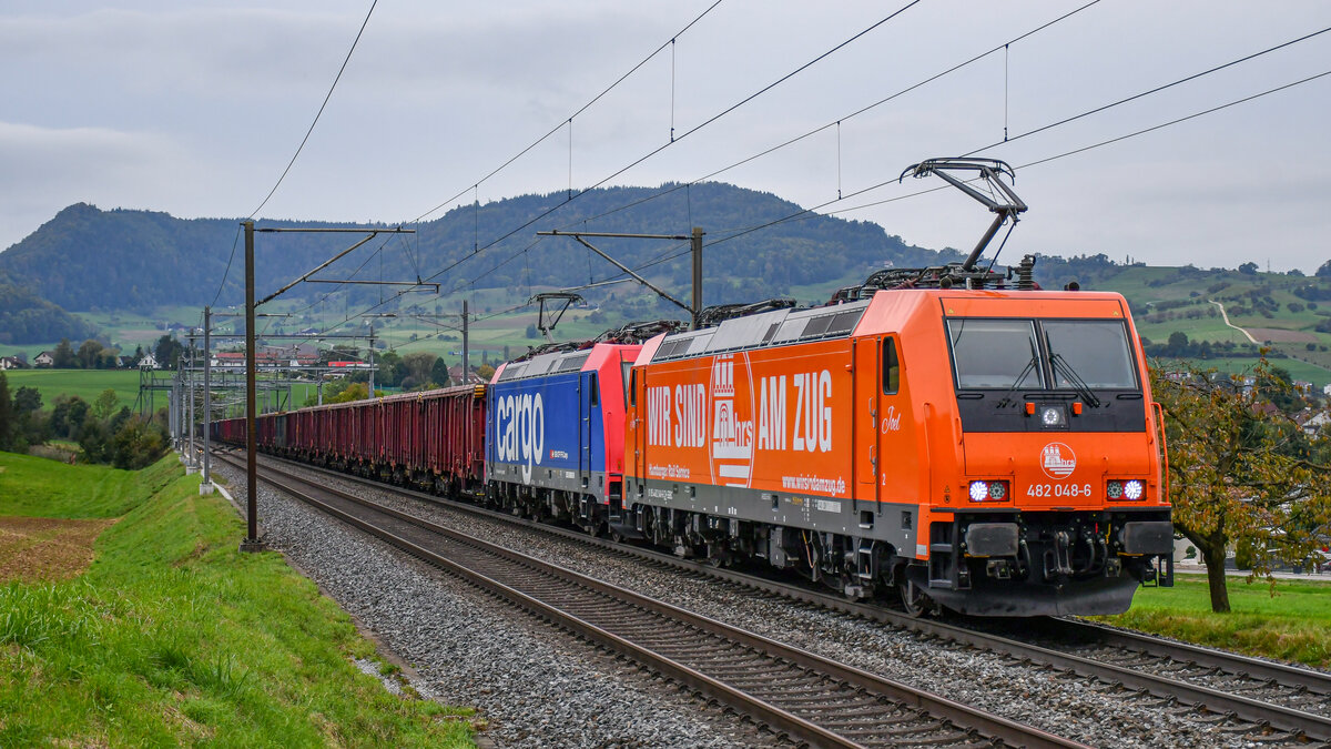 Rübenkampagne 2021: Re 482 048-6 und 041-1 sind mit einem voll beladenen Rübenzug in Richtung Frauenfeld (CH) unterwegs, aufgenommen bei der Steigung nach Frick AG am Abend des 03.10.2021.