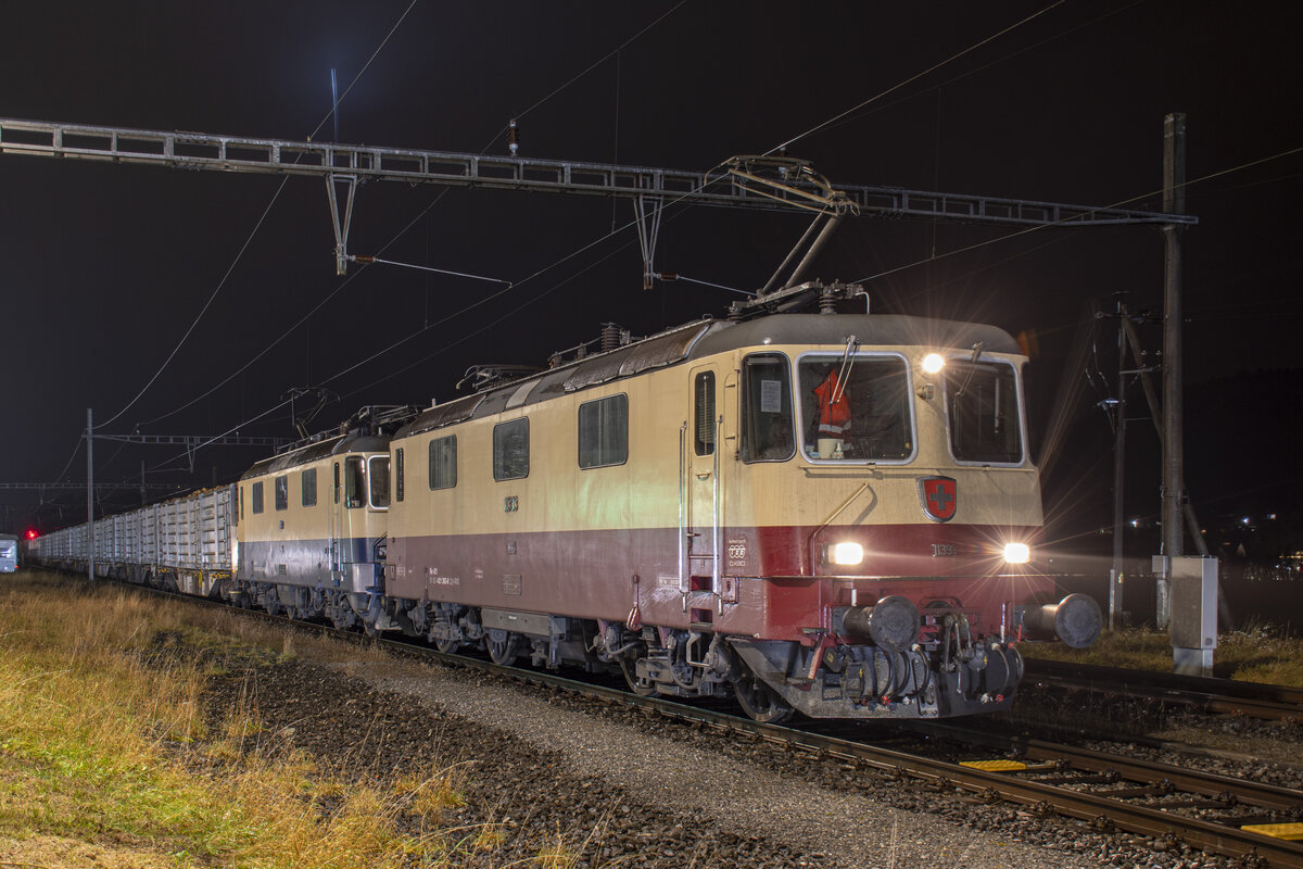 Rübenkampagne 2021: Trans Rail Re 4/4 11393 und 11387 warten mit einem vollen Rübenzug aus Koblenz in Weiach-Kaiserstuhl eine Kreuzung ab, aufgenommen am Abend des 08.12.2021.