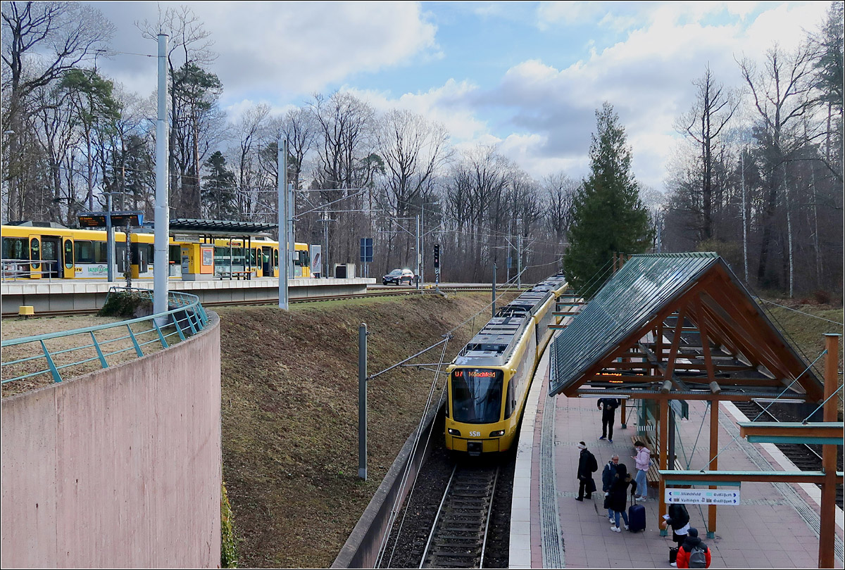 Ruhbank - die Haltestelle auf zwei Ebenen - 

Ursprünglich war es gar nicht vorgesehen die alte oberirdische Strecke der Straßenbahnlinie 15 über die Gänsheide mit Stadtbahnwagen zu befahren. Als Ersatz wurde 1998 die vom Weinsteigetunnel abzweigende Tunnelstrecke über die Waldau zur Ruhbank gebaut, wo 1999 die bestehende Strecke nach Heumaden angebunden wurde, wobei auch in Sillenbuch ein Stadtbahntunnel entstand. Im Jahr 2000 wurde diese Strecke von Heumaden über Ruit nach Ostfildern verlängert.
Bis 2007 wurde dann aber doch die steile und über eine weite Strecke in der Straße verlaufende Strecke vom Olgaeck über die Gänsheide ausgebaut. Die Tunnelstrecke über die Waldau macht aber dennoch Sinn, da so die Fahrtzeit in die Innenstadt verkürzt hat, auch im Hinblick auf die Verlängerung nach Ostfildern-Nellingen. Zudem sind dadurch auch Doppeltraktionen möglich.

Im Bild links eine Bahn der Linie U15, die außerhalb der HVZ hier endet und unten ein Zug der U7, der hier nach dem Halt im Tunnel verschwinden wird.