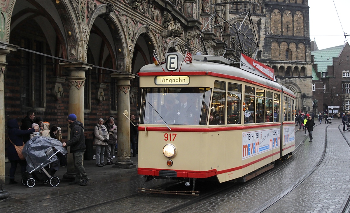 Rund um Markt und Dom befindet sich der Bremer Weihnachtsmarkt, der am ersten Adventssonntag, dem 27.11.2022, trotz des einsetzenden Regens sehr gut besucht war. Eine wegen der zahlreichen die Schienen kreuzenden Passanten weder für den Straßenbahnfahrer noch für den Fotografen ganz einfache Situation. Der 1957 in Dienst gestellte GT3 917 fährt gerade an den Rathausarkaden vorbei. Er gehört zu einer Serie von 20 Fahrzeugen, die als erste Gelenkwagen im Bremen verkehrten. Den zweiachsigen Triebwagen baute die Bremer Straßenbahn in Eigenregie, Hansa-Waggon lieferte die einachsigen Nachläufer. 1977 wurden die Fahhrzeuge abgestellt.