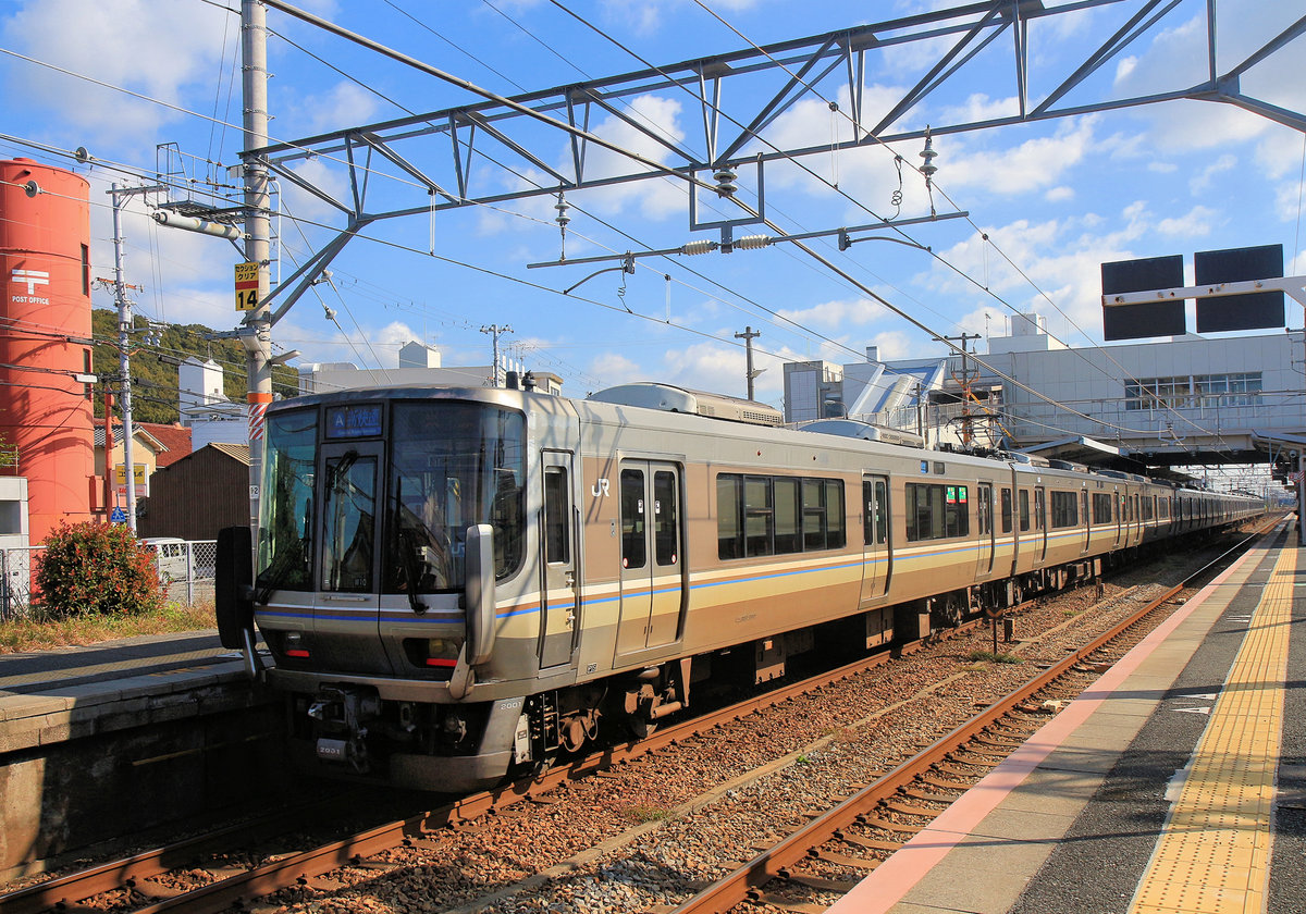 S-Bahnzüge Serie 223 für die Region Kansai (das Gebiet um Kyôto – Ôsaka – Kôbe); Gleichstrom 1500 V. Diese Züge haben nur 3 Seitentüren (Züge für Halt an allen Stationen haben 4) und bequeme Hintereinander-Sitze mit in Fahrtrichtung umklappbaren Rückenlehnen (Züge für Halt an allen Stationen haben Längssitze). Serie 223 ist vor allem für Eilzüge bestimmt und bildet auch das Rückgrat der  Neuen Eilzugsdienste , das sind schnelle durchgehende, aber zuschlagsfreie Züge durch das ganze Kansai-Gebiet. Es gibt insgesamt 927 Wagen, nämlich 121 4-Wagenzüge, 14 6-Wagenzüge und 39 8-Wagenzüge, dazu einen Diensttriebwagen. Baujahre 1995-2008. Von demselben Typ Serie 223 gibt es überdies 16 Zweiwagenzüge für die ländlichen Strecken im Bergland zwischen dem Kansai und dem Japanischen Meer (Serie 223-5500), sowie 7 Zweiwagenzüge (Serie 223-5000), die mit einem ähnlichen 3-Wagenzug von JR Shikoku (JR Shikoku Serie 5000) gekuppelt den Pendelverkehr über die Grosse Seto-Brücke auf die Insel Shikoku hinüber besorgen. Im Bild ein 8-Wagenzug (westseitiger Steuerwagen KUHA 222-2001) + ein 4-Wagenzug davor in Aboshi, 6.November 2018.  SANYÔ HAUPTLINIE 

