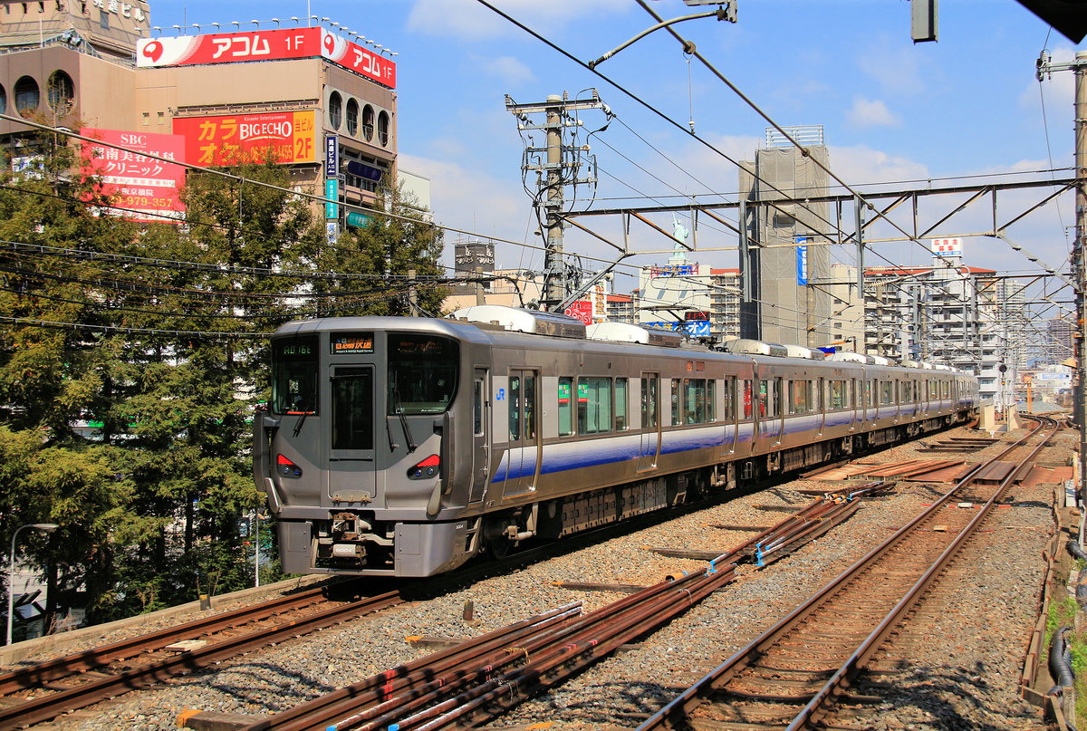 S-Bahnzüge Serie 225 für die Region Kansai (das Gebiet um Kyôto – Ôsaka – Kôbe); Gleichstrom 1500 V. Diese Züge haben nur 3 Seitentüren (Züge für Halt an allen Stationen haben 4) und bequeme Hintereinander-Sitze mit in Fahrtrichtung umklappbaren Rückenlehnen (Züge für Halt an allen Stationen haben Längssitze). Die Serie 225 ist die Nachfolgerin derSerie 223; seit 2010 wurden 372 Wagen gebaut (eingereiht als 51 4-Wagenzüge, 16 6-Wagenzüge und 9 8-Wagenzüge). Im Bild ist Zug 225-5004 von 2010; er verbindet gerade die Ôsaka-Ringbahn mit dem Internationalen Flughafen Kansai. Kyôbashi(in der Stadt Ôsaka), 28.März 2017  ÔSAKA RINGBAHN / HANWA LINIE / KANSAI FLUGHAFENLINIE  