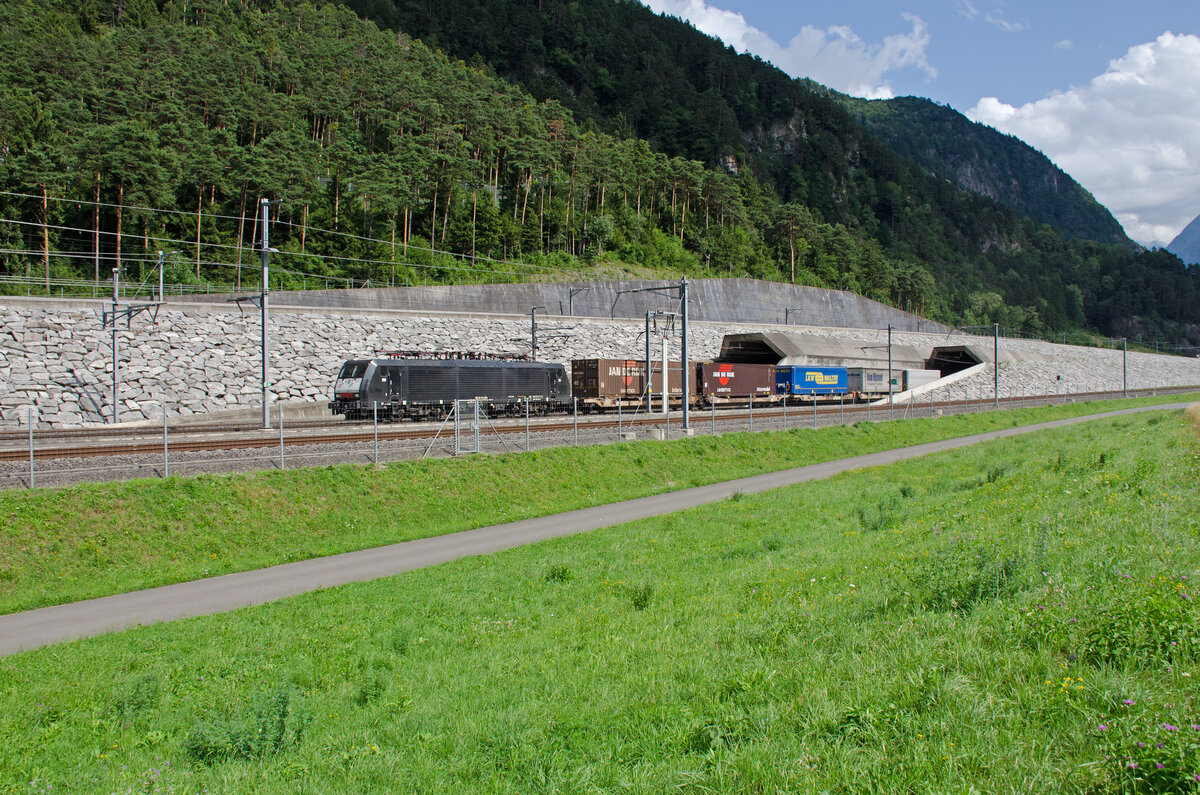 Samstag den 22.07.2023 um 16:36 Uhr am Gotthard-Basistunnel Nordportal. Die linke Röhre ist die Oströhre (in der Regel für den Nord-Südverkehr) während die rechte Röhre, die Weströhre (in der Regel für den Süd-Nordverkehr) benützt wird. Hinter der Oströhre an der Mauer entlang führt die alte Strecke von Altdorf über Erstfeld nach Göschenen. Während das Gleis vorne an der Weströhre die alte Strecke von Göschenen über Erstfeld nach Altdorf ist. Die Tunnellänge des GBT beträgt 57,1 km. Die Ansicht zum Portal ist in Nord- Südrichtung. Vom Süden her ausfahrender Güterzug aus der Weströhre. Bei dem Bild geht es ausnahmsweise nicht um die Züge sondern um die Vorstellungskraft was es bedeutet während bis zu 12 Minuten (bei Güterzügen noch länger) sich in einem Tunnel zu befinden. Ohne sich klar zu werden ob die Dunkelheit jemals endet. Da ich diesen Tunnel schon oft befahren habe, und dabei Ortsfremde Reisende (vor allem aus dem Ausland) immer wieder beobachten kann wie sie etwas Unruhig werden wen nach zirka 10 Minuten immer noch kein Tageslicht zu erblicken ist, dann ist es schon beeindruckend was da geschaffen wurde. Wer das Buch „Der Tunnel“ von Friedrich Dürrenmatt (1952) oder „Der Tunnel“ von Hans Leister welcher in seinem Buch den Gotthard-Basis-Tunnel meint und die Handlung darin sogar in diesem Tunnel stattfindet, der versteht vielleicht meinen  Grund für diese Aufnahme. Hans Leister verweist dabei sogar auf die Ausgabe von Dürrenmatt aus dem Jahre 1952. Der versteht vielleicht den Grund für das Bild. Aber eben, erst wen man mindestens eines der Bücher oder sogar beide gelesen hat. Leider sind die Portale nicht so schön wie die alten Portale. Es gibt auch einen technischen Grund dafür. Koordinaten GMS (Grad, Minuten, Sekunden): N 46° 50’ 11.9’’ O 8° 38’ 43.8’’