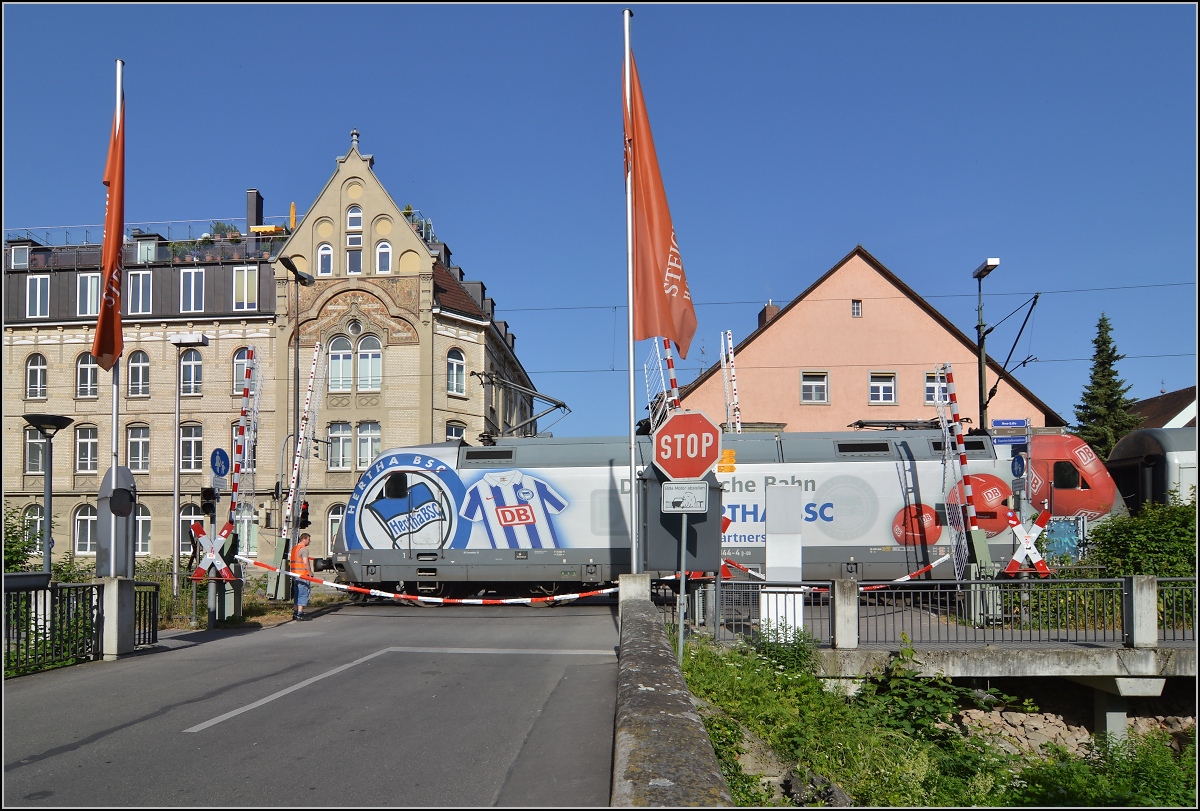 Sandwich mit zwei bunten Enden. 101 144-4 mit Herta BSC-Werbung am gestörten Bahnübergang vor dem Inselhotel Konstanz. Juni 2014.