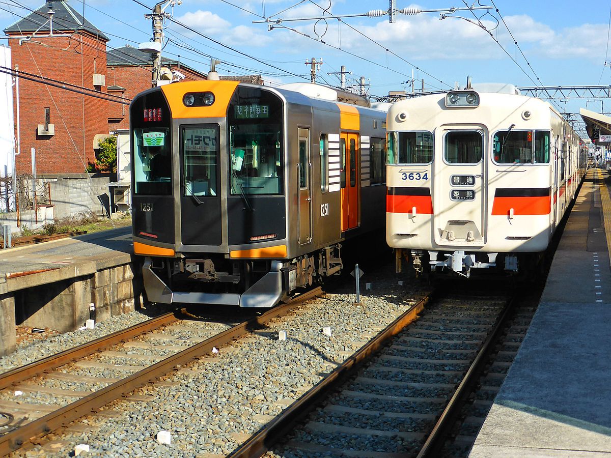 Sanyô-Konzern: In der Station Ôshio steht der alte Sanyô-Lokalzug 3058 (...3634), während ein Expresszug (Nr. 1201, Baujahr 2006) des Hanshin-Konzerns von Himeji Richtung Osaka vorbeibraust. Diese schönen Hanshin-Züge fahren über Osaka hinaus etwa 30 km bis in die alte Kulturstadt Nara über die Strecke des Kintetsu-Konzerns. 22.März 2014. 