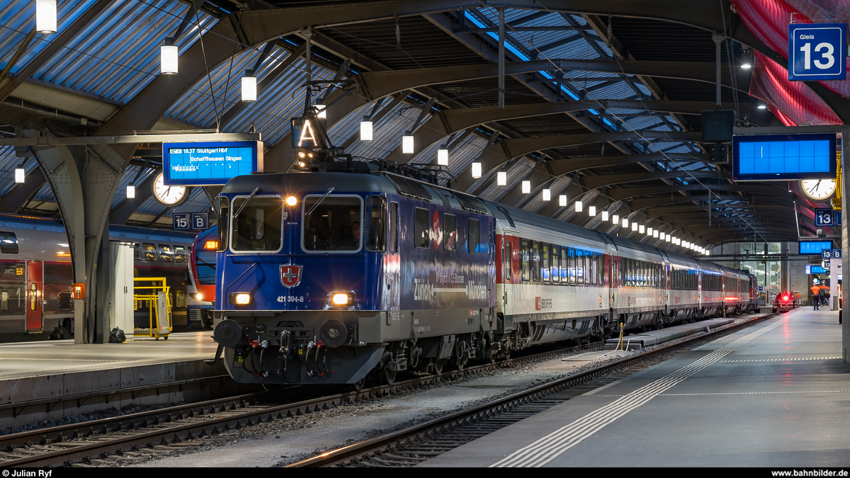 SBB Cargo Re 421 394 mit Werbung für die ab (Dezember) 2021 beschleunigte Bahnverbindung Zürich - München am 8. März 2020 in Zürich HB vor einem IC nach Stuttgart.
