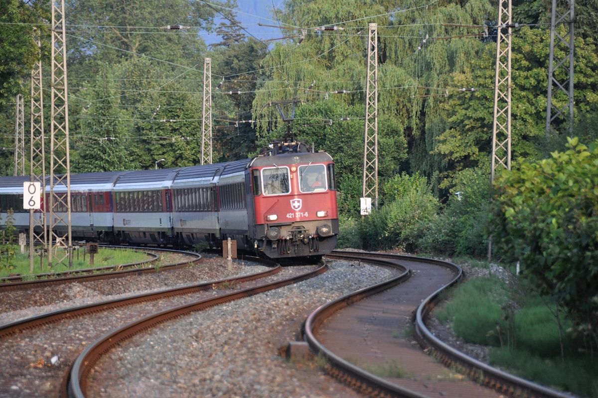 SBB Re 421 371 = Umbau der neuesten Serie der Re 4/4II (in Deutschland zugelassen) der SBB Cargo vor dem EuroCity Zürich-München am 20.07.2013 bei der Bahnhofseinfahrt Lindau vor dem Bahnübergang Hasenweidweg / am Alpengarten