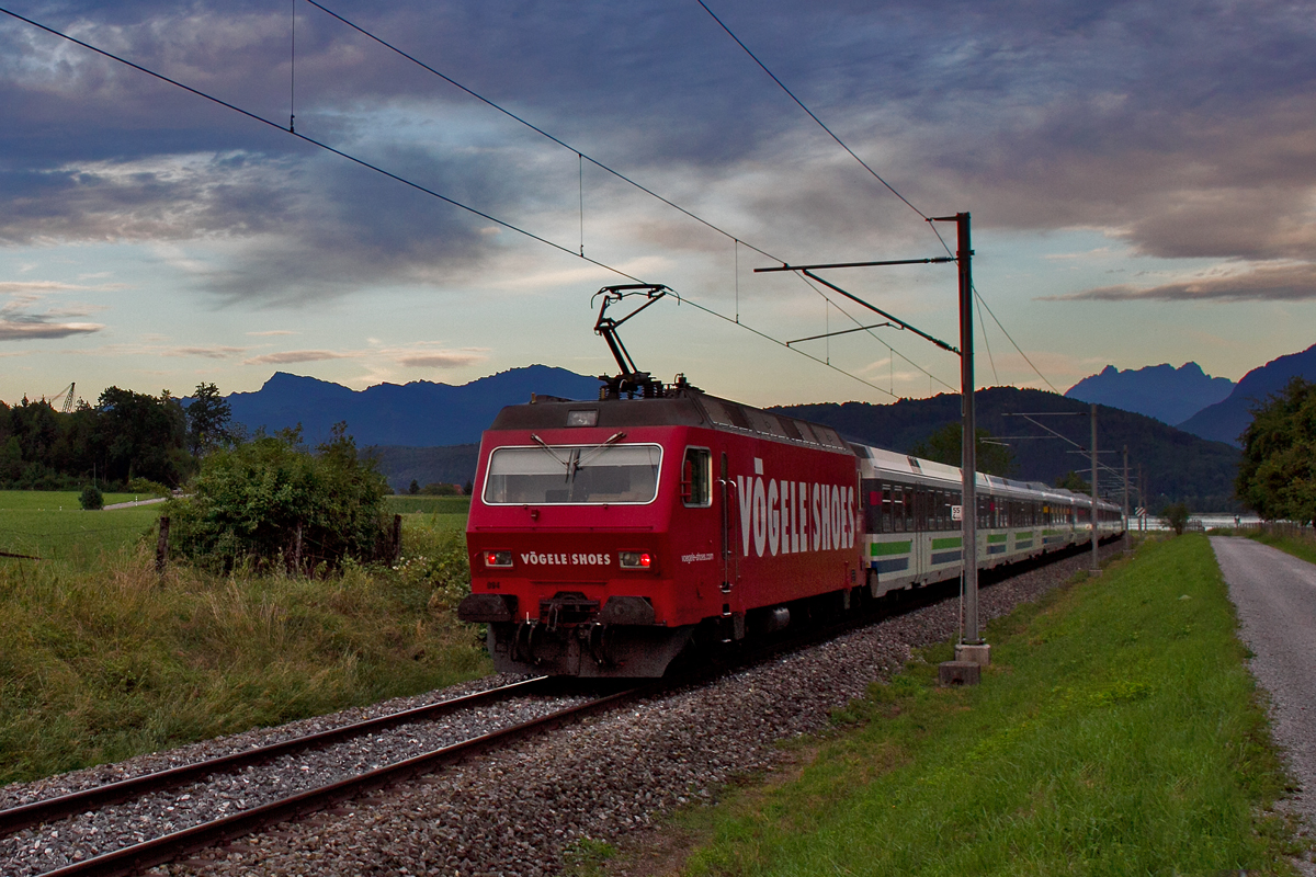 Schiebende Werbelok  Vögele Shoes  Re 446 094 fährt bei einer leichten Föhnstimmung in der Dämmerung mit dem Voralpenexpress in Bollingen vorüber.Bild vom 31.7.2015
