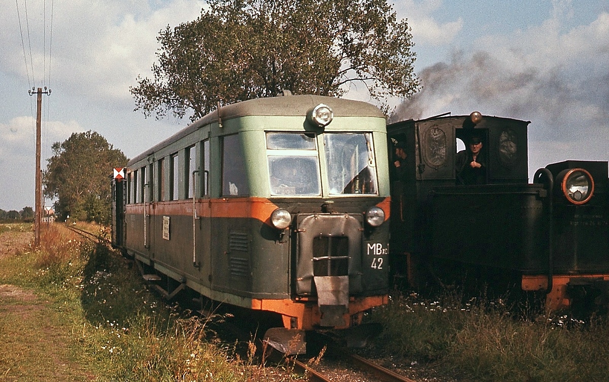 Schmalspurbahnen in Polen: Der bereits gezeigte MBxc1 42 der 600 mm-spurigen Jarotschiner Kreisbahn am 25.09.1976 bei der Zugüberholung in Twardow Mianka. Der Triebwagen führt sogar noch einen Güterwagen mit sich. Das Fahrzeug lieferte Lilpop, Rau i Löwenstein in Warschau im Jahre 1934, hier wurden neben Triebwagen auch Straßenbahnfahrzeuge und Kfz gebaut. Lt. einem Fahrplan 1973/74 benötigten die Züge für die 20 km von Robakow nach Witaszyce etwa 80 Minuten (z. B. verließ der erste Zug Robakow am Morgen um 03:50 Uhr und kam um 05:15 Uhr in Witaszyce an). Die Durchschnittsgeschwindigkeit von 15 km/h dürfte auch in Polen für damalige Zeit nicht sehr attraktiv gewesen sein, aber auf dem Land gab es keine Alternativen.
