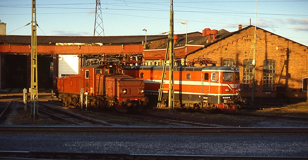 Schnappschuss aus dem Nachtzug von Narvik nach Stockholm auf eine unbekannte Hg sowie die Rc2 1104 vor dem Lokschuppen von Boden an der schwedischen Nordlandsbahn (Mai 1988)