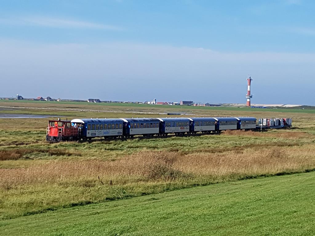 Schöma Lok 399108 kommt hier am 1.10.2017 mit einem Personenzug vom Hafen Wangerooge und wird in Kürze das Deich Tor erreichen. Im Hintergrund ist der neue Leuchtturm der Insel zu sehen.