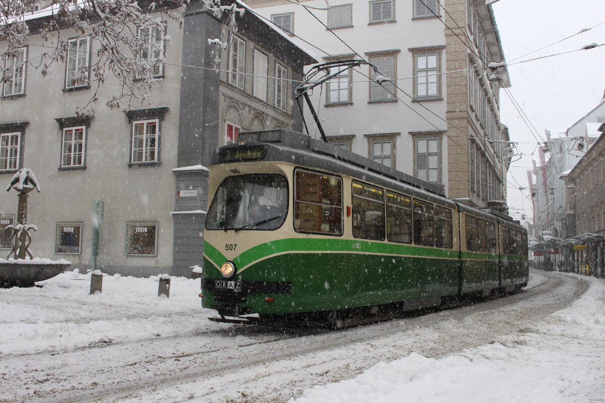 Schon in der Nacht von 8.12. auf 9.12.2021 schneite es in der steirischen Landeshauptstadt kräftig und am 9.12. kam reichlich Schnee dazu.
Der von SGP gebaute Wagen 507 von Typ  Mannheim  steht am 9.12.2021 bei dichtem Schneefall in der Haltestelle Schloßbergplatz/Murinsel.