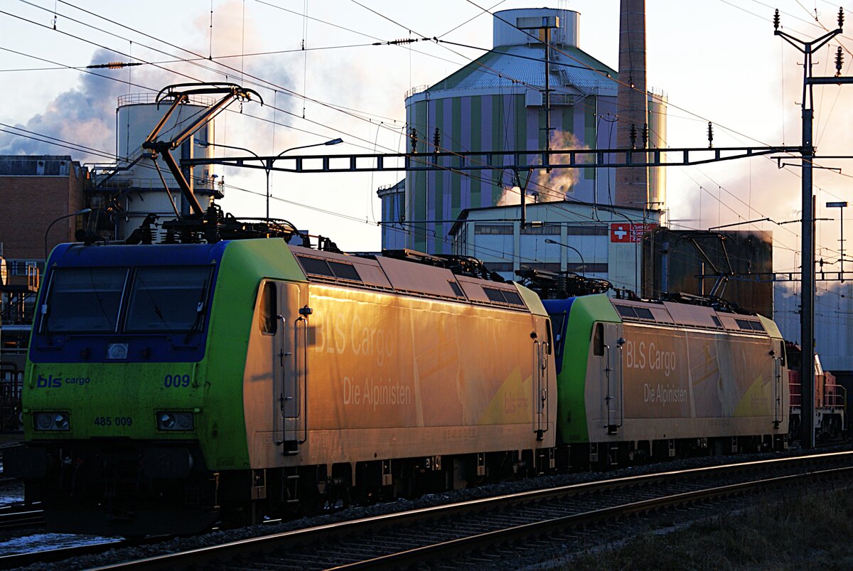Schweizer Zucker AG, Zuckerfabrik Aarberg, Kampagne 2025: Re 485 010-3 + Re 485 009-5, im Hintergrund Bauten der Zuckerfabrik, Aarberg, 5. Januar 2026. Die letzte Fuhre Zuckerrüben vom Verladeort Chavornay ist abgeliefert, im letzten Sonnenlicht des Tages,  ... wenn d'Sunnä hingerem Jura ungergeit ... , rollen die Loks auf das Lokabstellgleis, um auf den nächsten Einsatz zu warten. 
