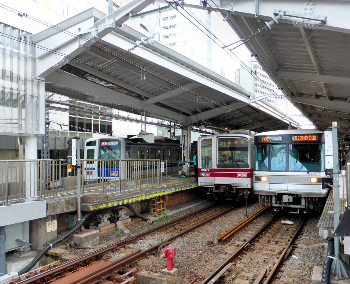 Seibu Konzern / Tôbu Konzern / Tôkyô Metro: Im Bahnhof des Tôkyû-Konzerns in Naka Meguro, Tokyo, wartet am 18.Oktober 2013 rechts ein U-Bahnzug der Hibiya-Linie (Nr. 03-132); wenn er nördlich von Tokyo an die Oberfläche kommt, wird er als Kurszug des Tôbu-Konzerns weiterfahren. Daneben steht Zug 21872 (8.Wagen Nr.28872) des Tôbu-Konzerns, der umgekehrt von seinem Netz im Norden von Tokyo her als Kurszug der U-Bahn gekommen ist. Ganz links (hinter dem Gitter) steht Zug 6053 (Serie 6000) des Seibu-Konzerns; dieser wird nun als Kurszug des Tôkyû-Konzerns in die Stadt Yokohama (südlich von Tokyo) bis ins chinesische Viertel durchfahren. Leider muss für die Strecke jeder einzelnen Gesellschaft ein eigener Fahrpreis bezahlt werden, auch wenn die Züge durchfahren. Man kann das vor der Fahrt durch entsprechende Eingabe in den Automaten tun, oder aber mit einer einfachen Fahrkarte den Zug besteigen und am Endpunkt die Fahrkarte in ein Lesegerät stecken, der den genauen Fahrpreis ausrechnet. 