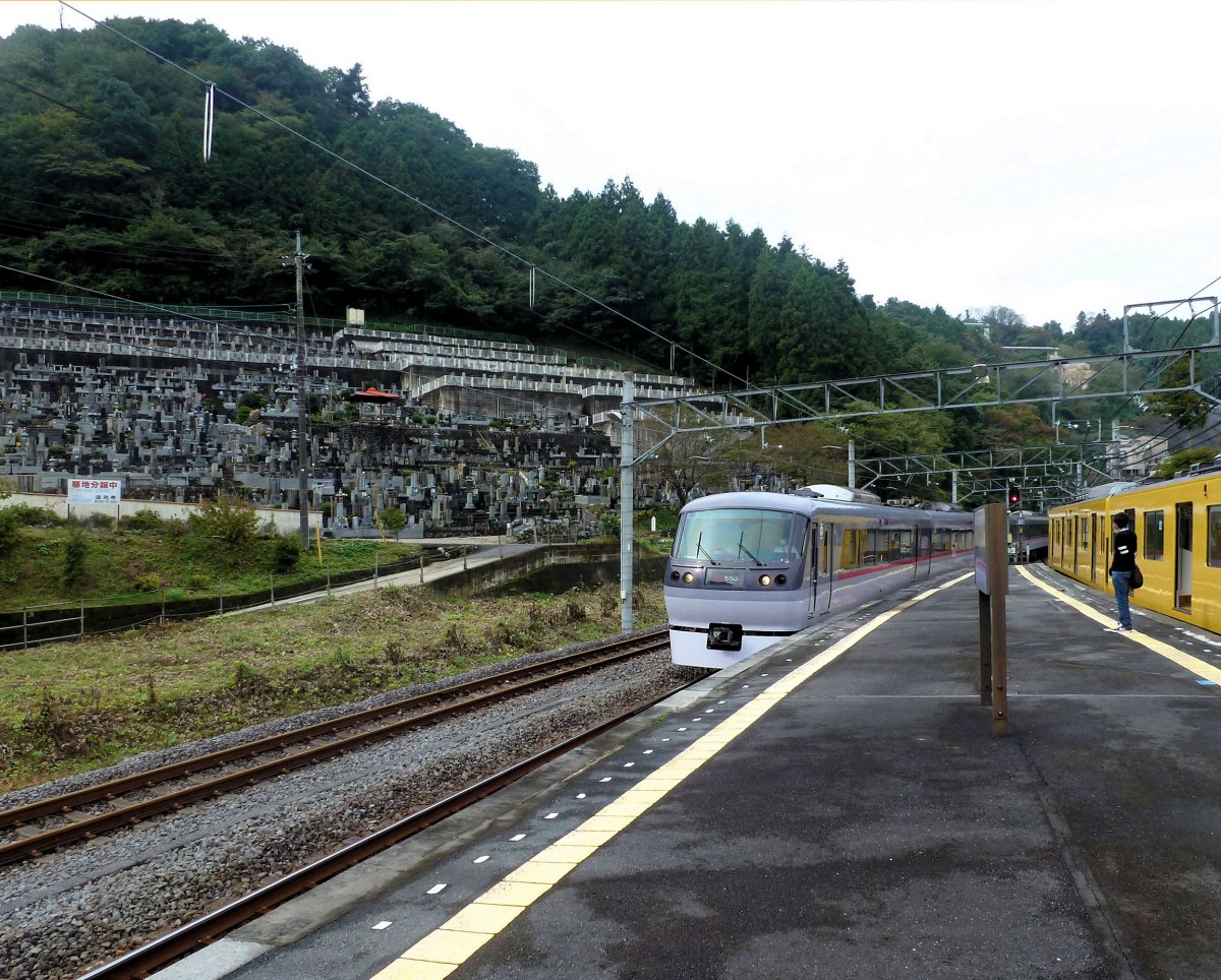 Seibu-Konzern, Chichibu-Linie: Während der S-Bahnzug 2069 in Agano wartet, kommt der Super-Express 10110 aus Chichibu entgegen. Auf ihren beiden Hauptlinien ab den grossen Bahnhöfen Shinjuku und Ikebukuro in Tokyo setzt der Seibu-Konzern auch Super-Expresszüge mit reservierten Sitzplätzen ein, die mit ganz wenig Zwischenhalten verkehren. Die 12 Siebenwagenzüge Serie 10000 wurden 1993-95 und 2003 beschafft; einer wurde 2007 vom Kaiser und dem schwedischen König benutzt. Im Hintergrund die grosse Grabanlage von Agano; eine Tafel dort besagt: Grab-Parzellen werden zum Kauf angeboten. 23. Oktober 2011. 