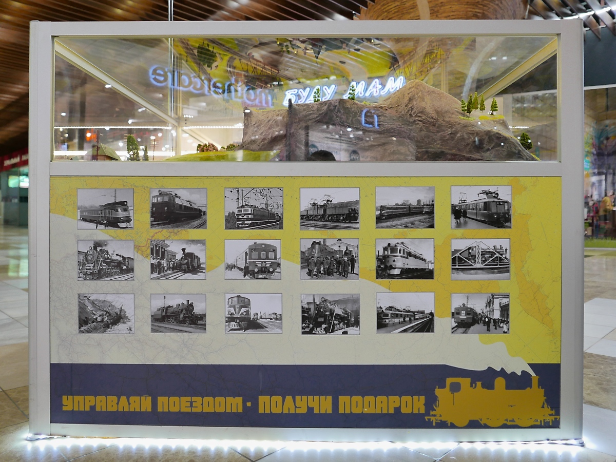 Seitenansicht der kleinen Modellbahn mit vielen historischen Bahnfotografien im Einkaufszentrum Piterlend in St. Petersburg, 17.2.18 

управляй поездом - получи подарок bedeutet in etwa: Steuere den Zug - erhalte ein Geschenk.