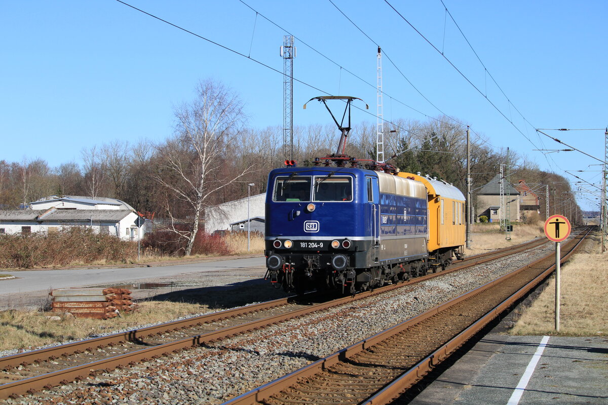 SEL 181 204 mit einem Begleiterwagen am 26.02.2022 auf der Fahrt von Mukran nach Neumünster. Die Lok brachte in der voherigen Nacht eine Lok der Baureihe 120 nach Mukran zur ich vermute mal Aufarbeitung bei BPSM. Aufgenommen am Haltepunkt Teschenhagen.