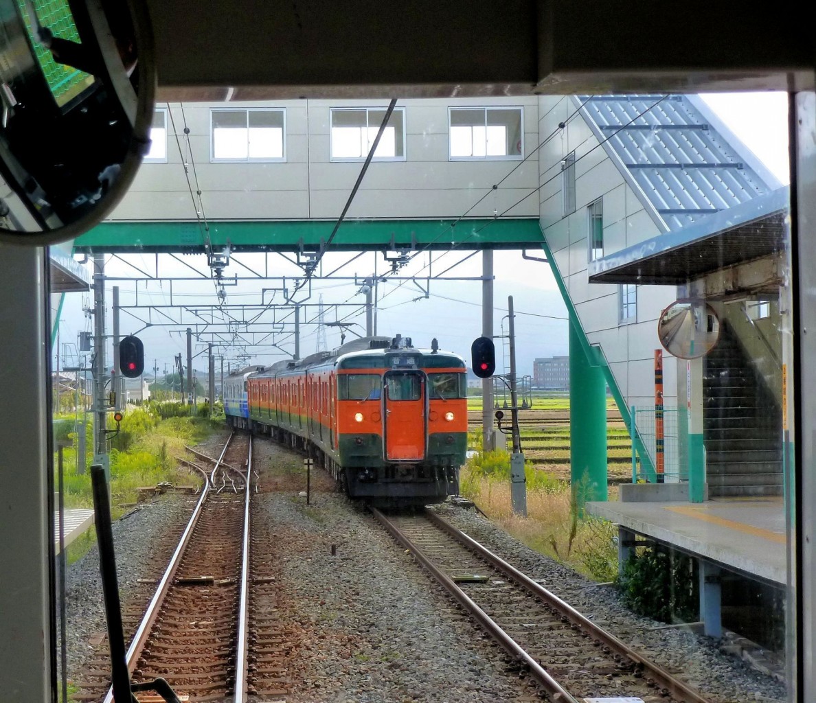 Serie 115 der Region Niigata: Einige Züge haben wieder ihren Originalanstrich dunkelgrün / orange bekommen. Hier Zug KUMOHA 115-1043 an der Spitze von zwei Dreiwageneinheiten bei der Einfahrt in Nishi Shibata. 18.Oktober 2011. Man beachte die Schutzweiche für die Ausfahrt in abweichender Stellung. (Aufnahme durch die verglaste Führerstandrückwand eines Gegenzugs) 