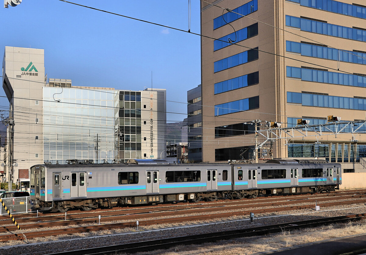 Serie 127 (E127), die hauptsächlichen Züge für den Betrieb in den zentralen Alpen. Der Typennummer wird ein E vorangestellt zur Kennzeichnung, dass der Wagen Eigentum von JR East Japan ist. Gleichstrom, 1995-1998 gebaut, 13 dieser Züge für den Bezirk Niigata (nur mit Längssitzen), 12 Züge für das Hochland von Matsumoto, die alle noch im Dienst sind. Im Bezirk Niigata schied 1 Zug nach Unfall aus, 10 wurden an eine Privatbahn verkauft, und die letzten 2 schieden 2022 aus. Die beiden Wagen werden bezeichnet als KUMOHA E127 (KU = mit Führerstand, MO = motorisiert, HA = gewöhnlicher Sitzwagen), und KUHA 126. Die meisten KUHA 126 tragen einen speziellen Enteisungsbügel (im Bild sichtbar). Im Bild steht Zug E127-111 in der Bergstadt Matsumoto, 10.April 2022  