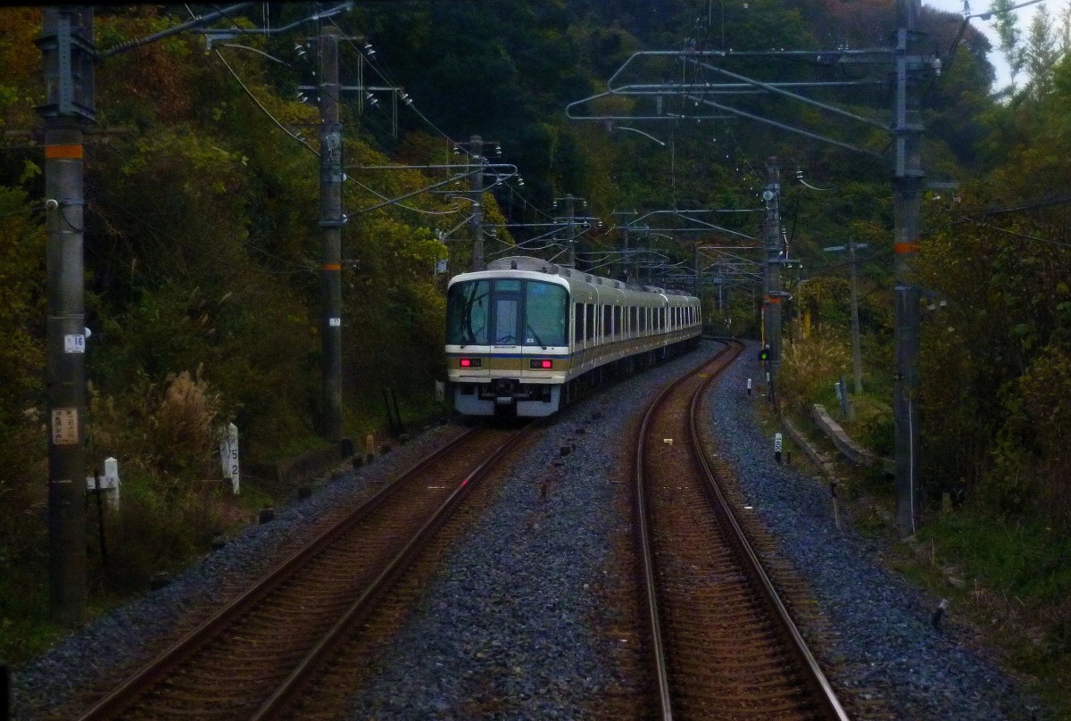 Serie 221: Im letzten Abendlicht kreuzen zwei Vierwagenzüge bei Sangô auf der Fahrt von Nara nach Osaka. Steuerwagen KUHA 221-23 am Schluss. 2.Dezember 2012. (Bild aus dem Rückfenster eines Gegenzugs)